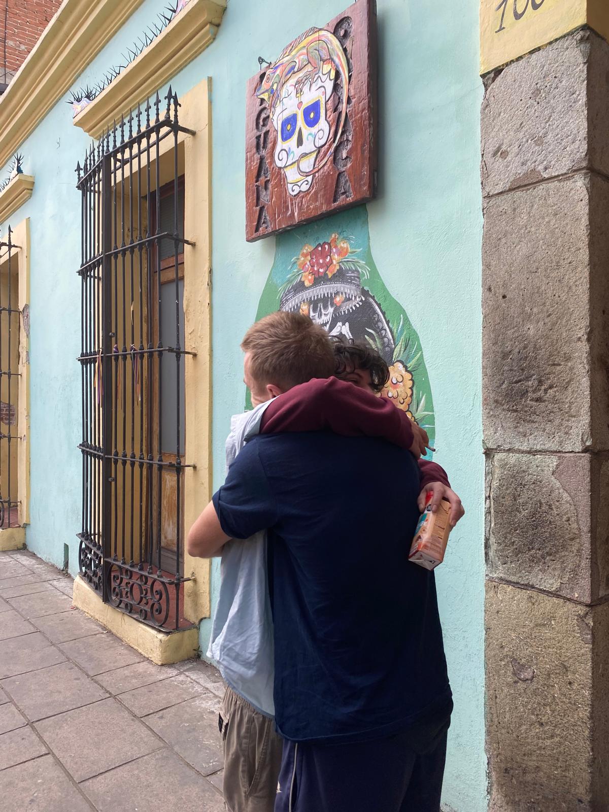 Two travelers hugging in front of a colorful wall in Oaxaca, Mexico